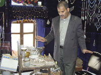 J e w e l e r M o h a m m e d A l i e x p l a i n s h o w t o c u t a n d p o l i s h o n y x . O n y x n e c k l a c e s a n d m e d a l s a r e d i s p l a y e d b e h i n d h i m .